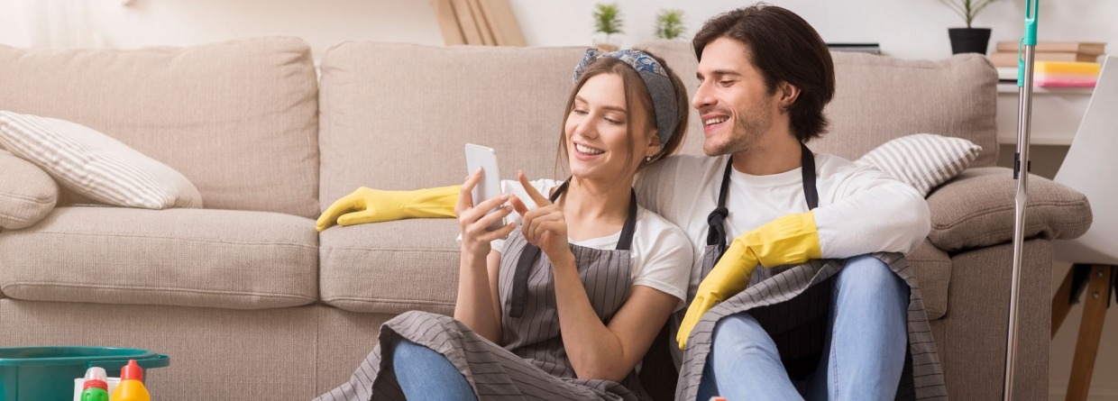 gelukkig stel kijkt tijdens het schoonmaken op de telefoon