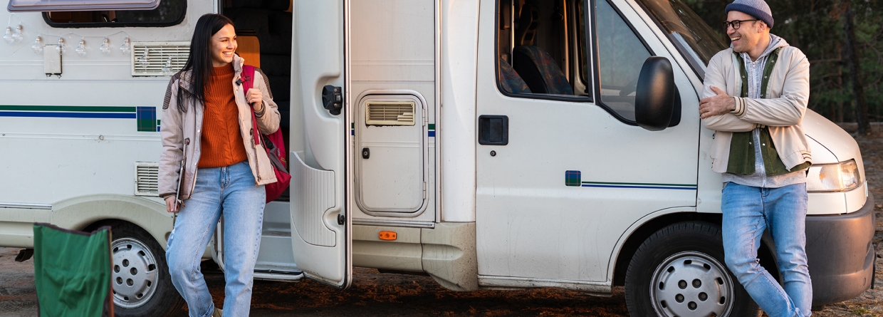 Vrouw komt uit camper in bosrijke omgeving en kijkt haar man vrolijk aan